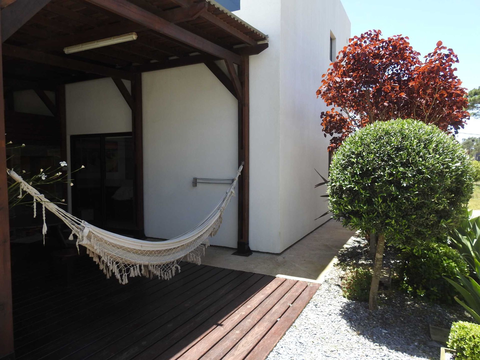 A hammock sits on a wooden deck in front of a house