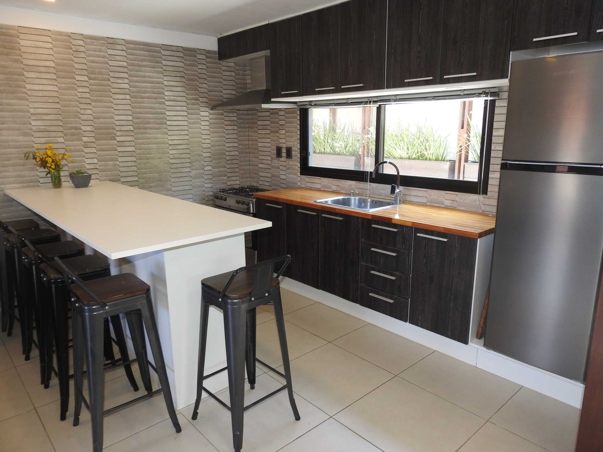 A kitchen with a stainless steel refrigerator , sink , table and stools