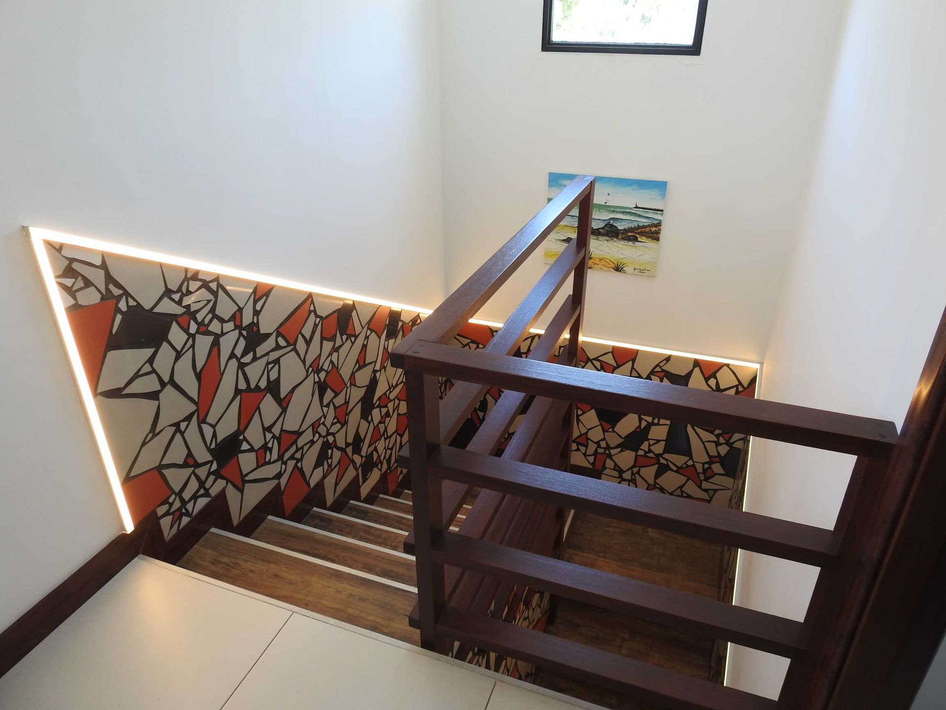 A staircase with a wooden railing and a painting on the wall