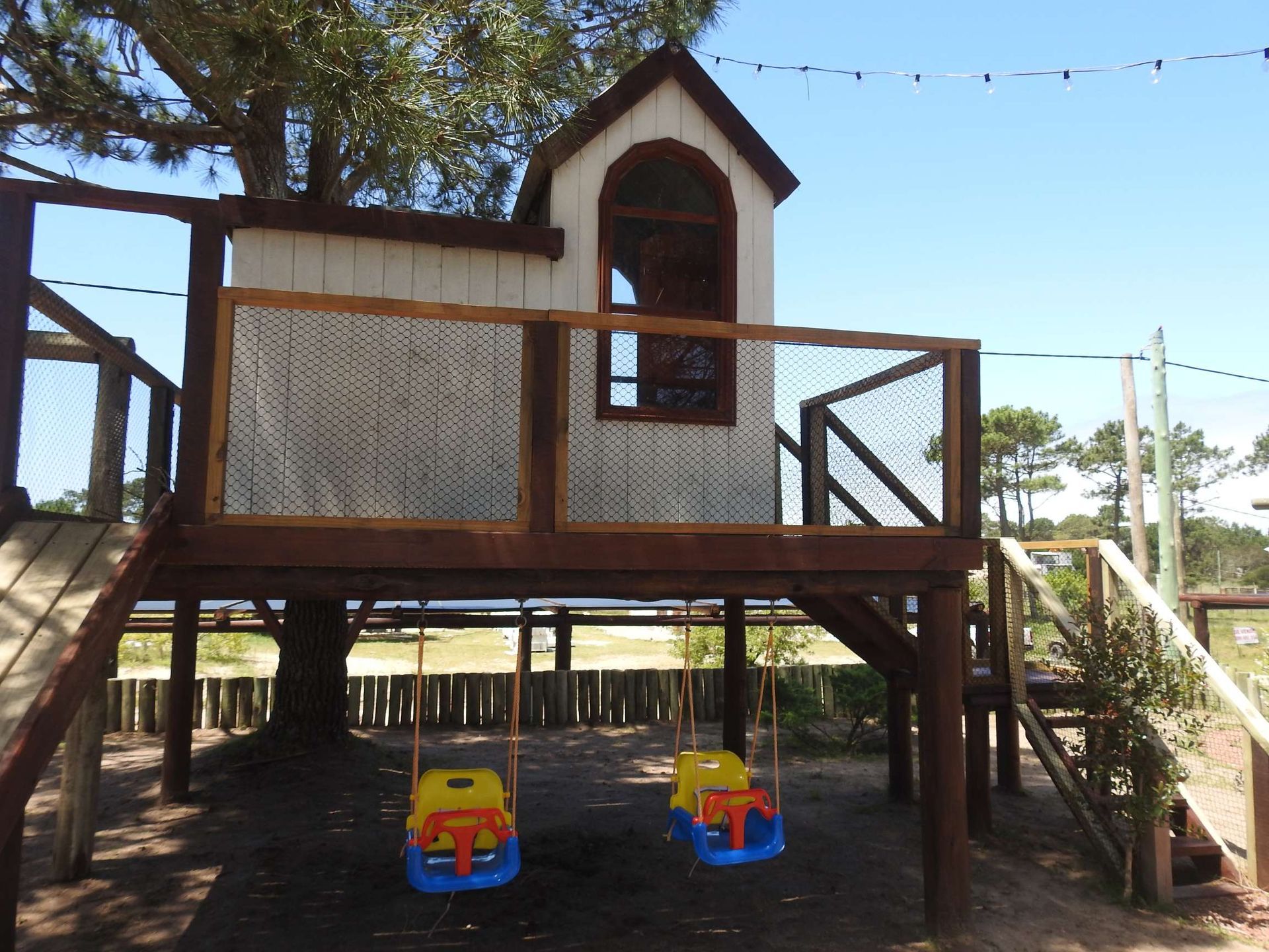A tree house with a slide and swings underneath it