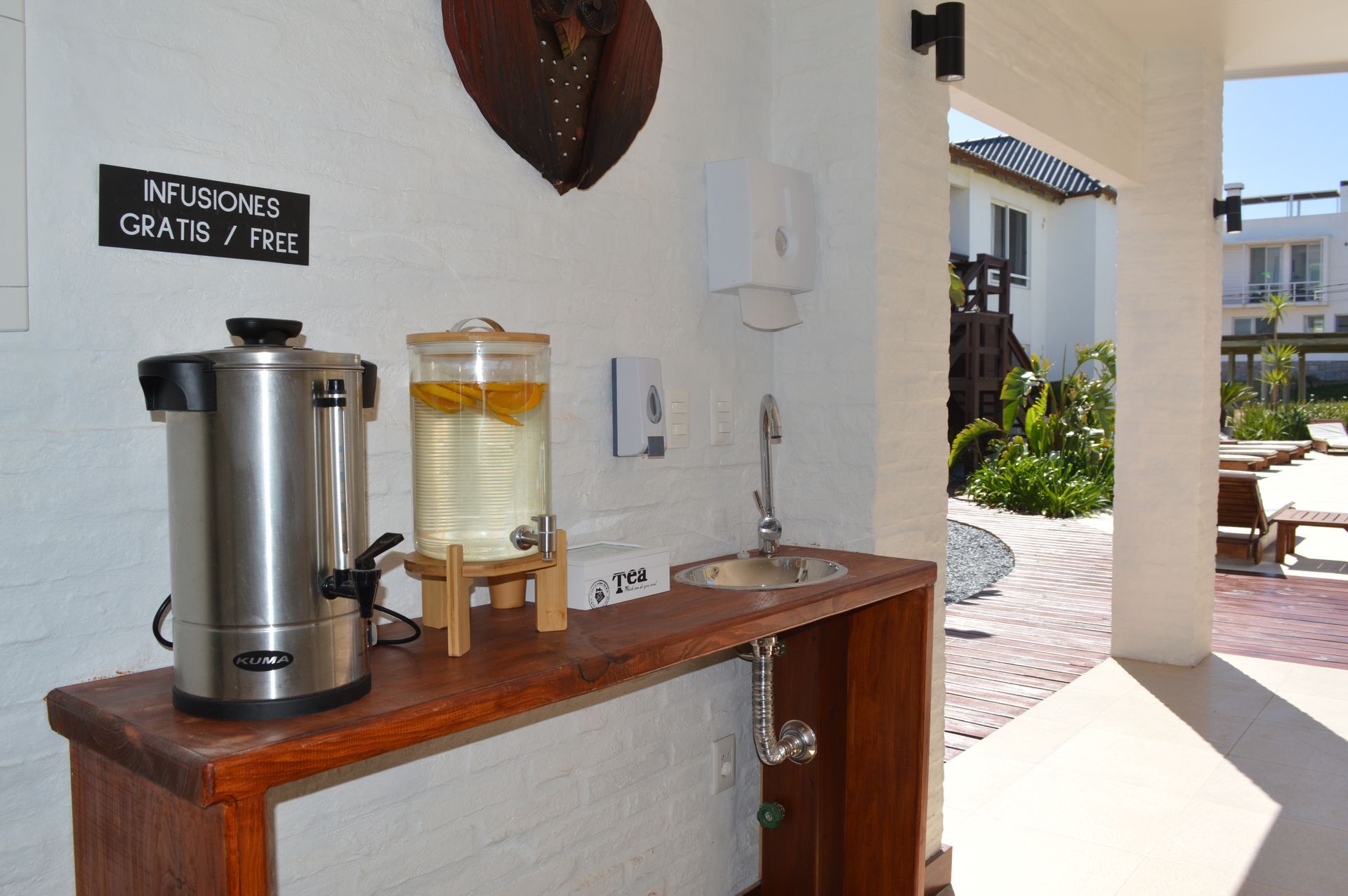 A stainless steel coffee maker is on a wooden counter next to a sign that says infusions created free