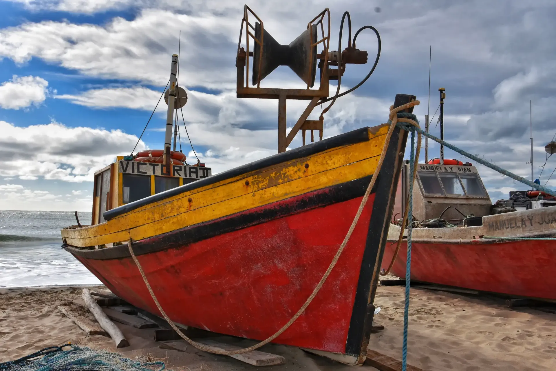 A red and yellow boat is tied to a pole on the beach.