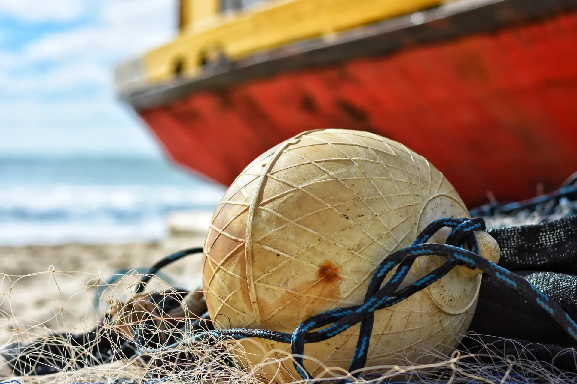 A fishing net and buoy on the beach with a boat in the background.