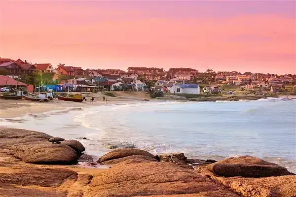 A beach with a pink sky in the background and rocks in the foreground.