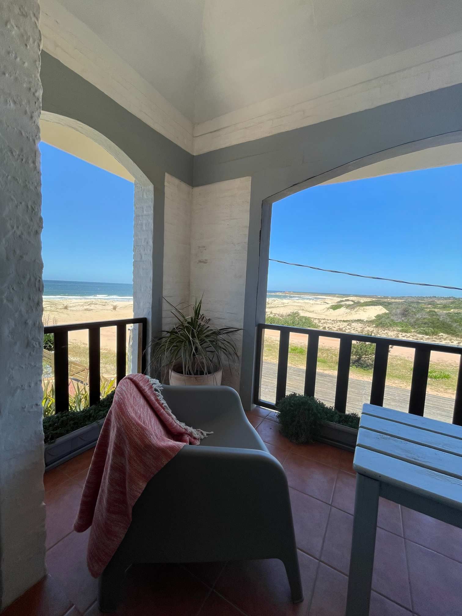 A balcony with a chair and a table with a view of the ocean.