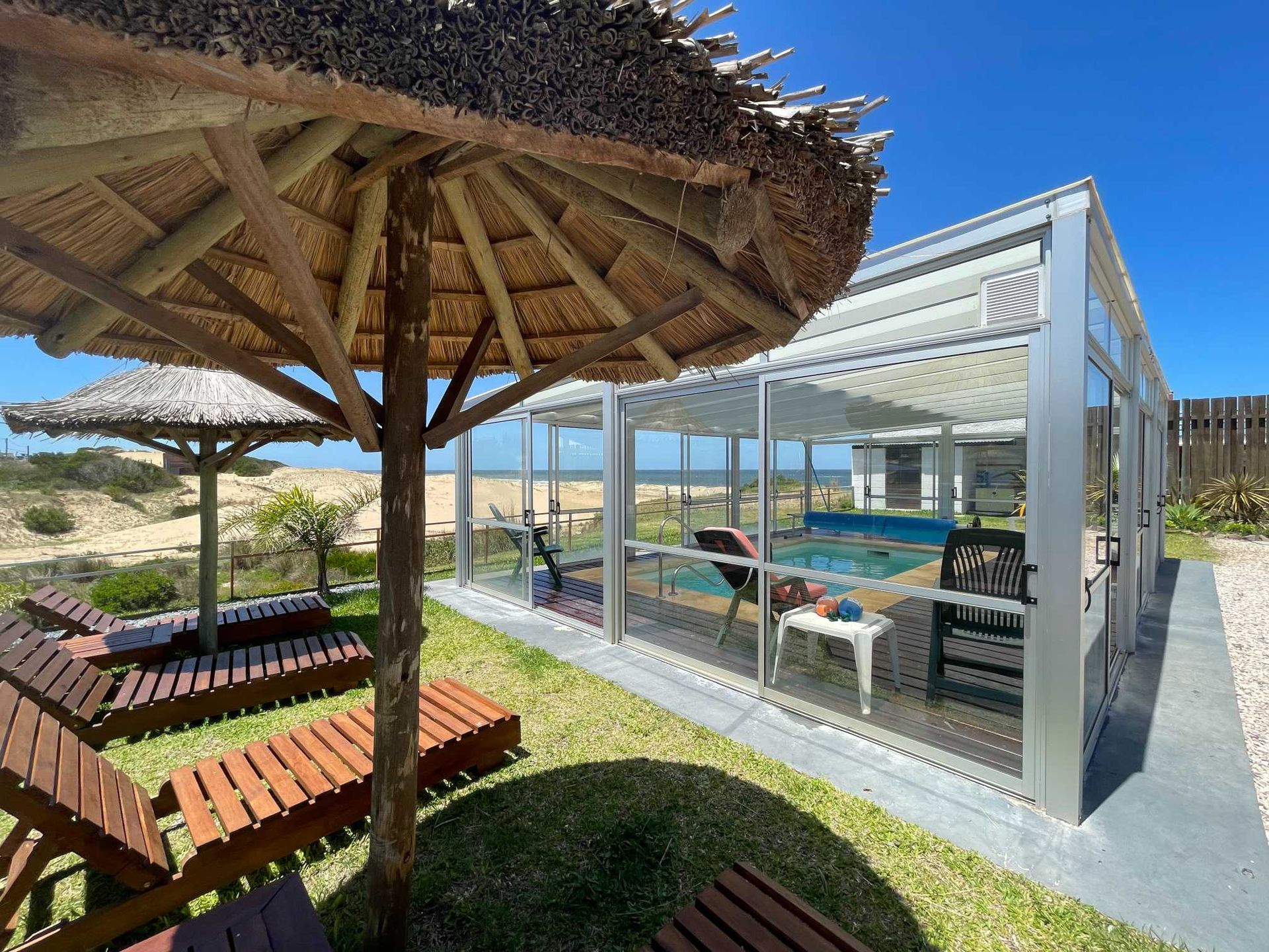 A thatched umbrella is sitting in front of a swimming pool.