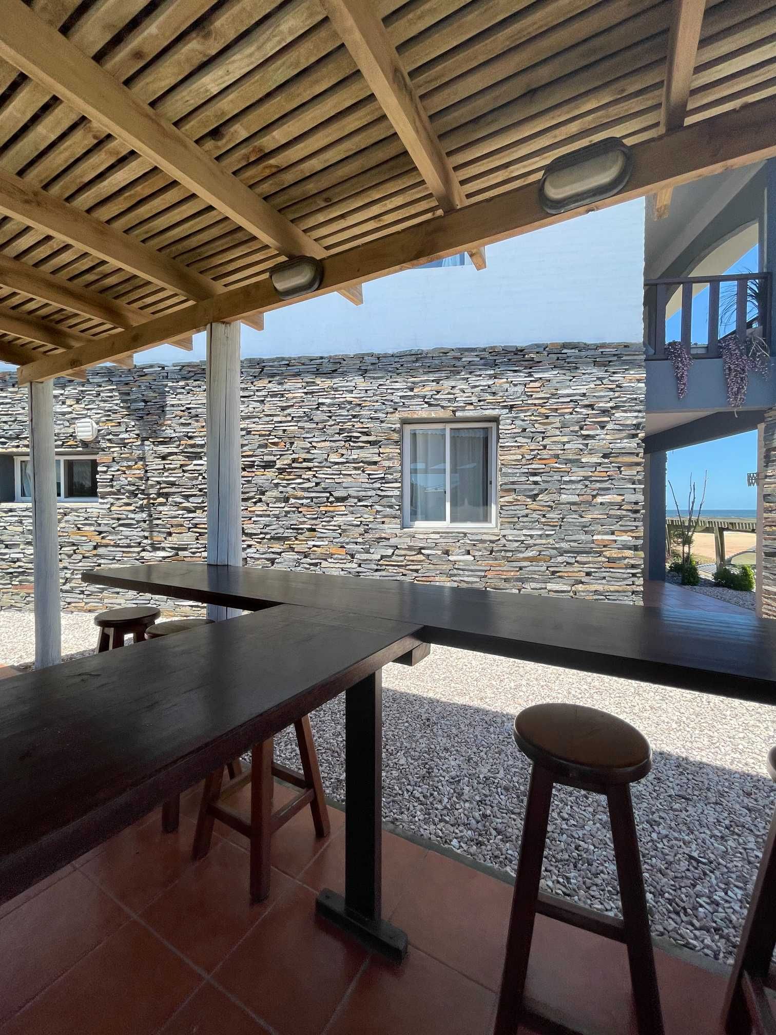 A patio with tables and stools under a wooden roof.