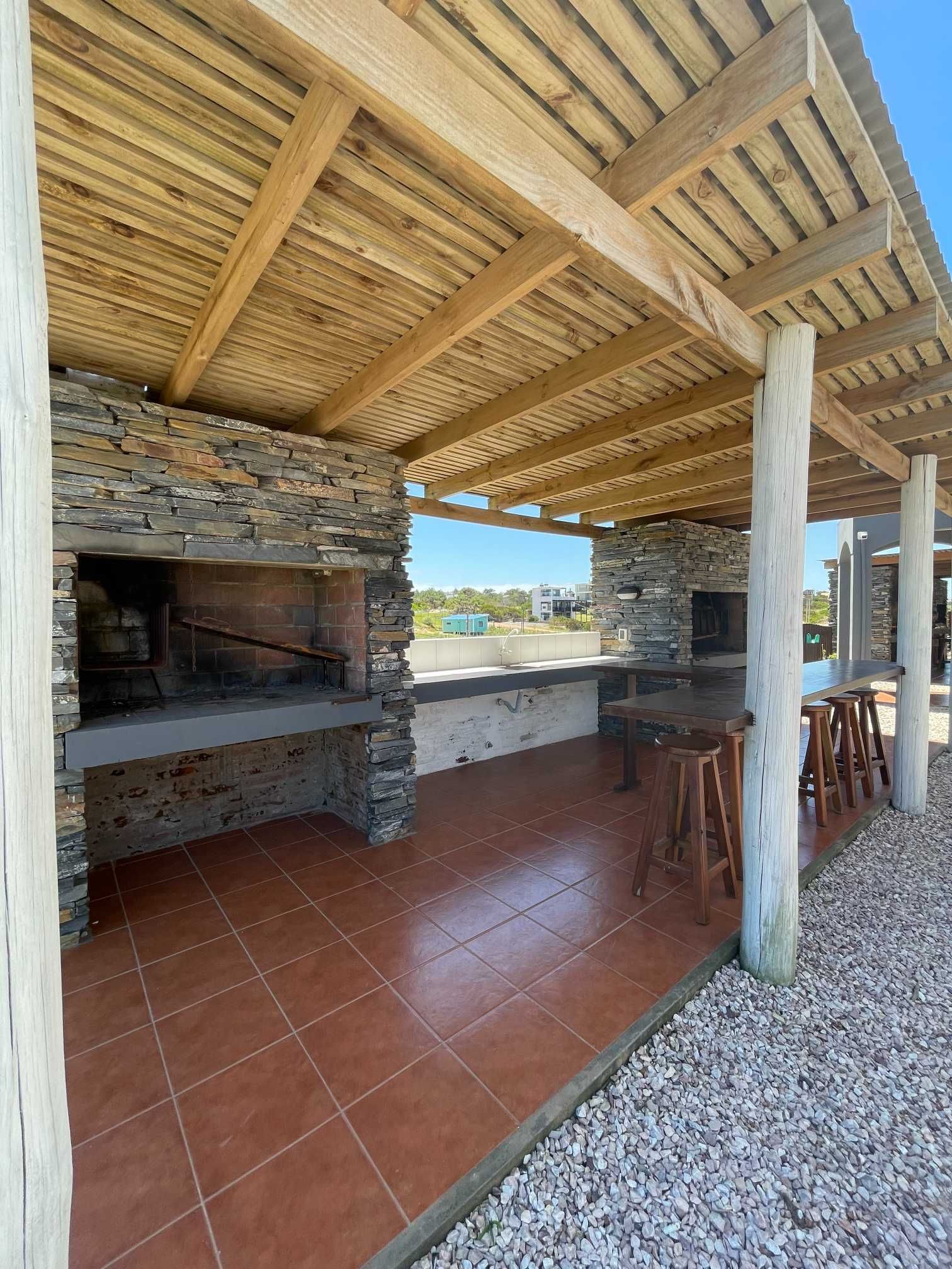 A covered area with a wooden roof and a grill.
