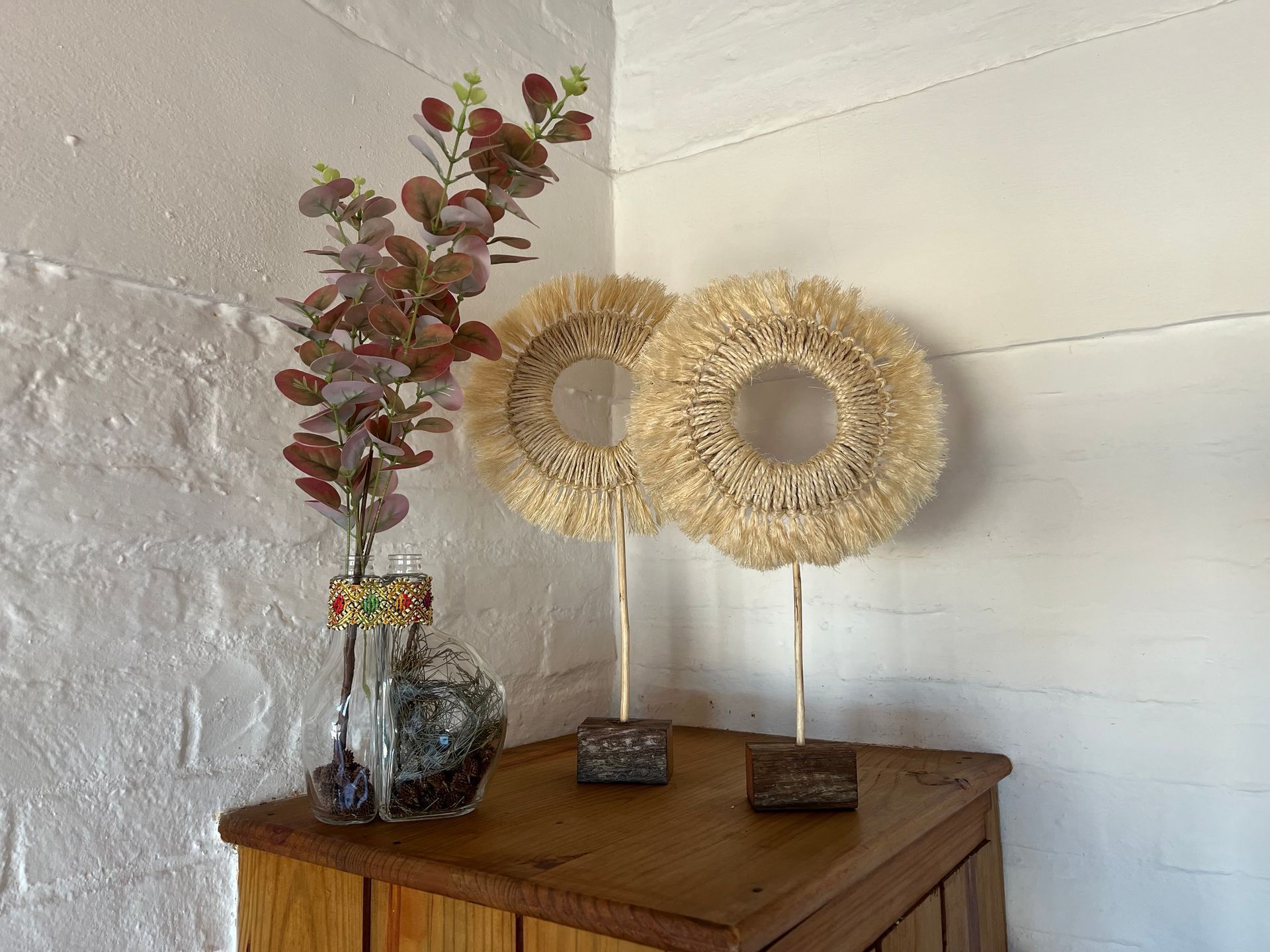 A vase of flowers is sitting on a wooden table next to two wreaths.
