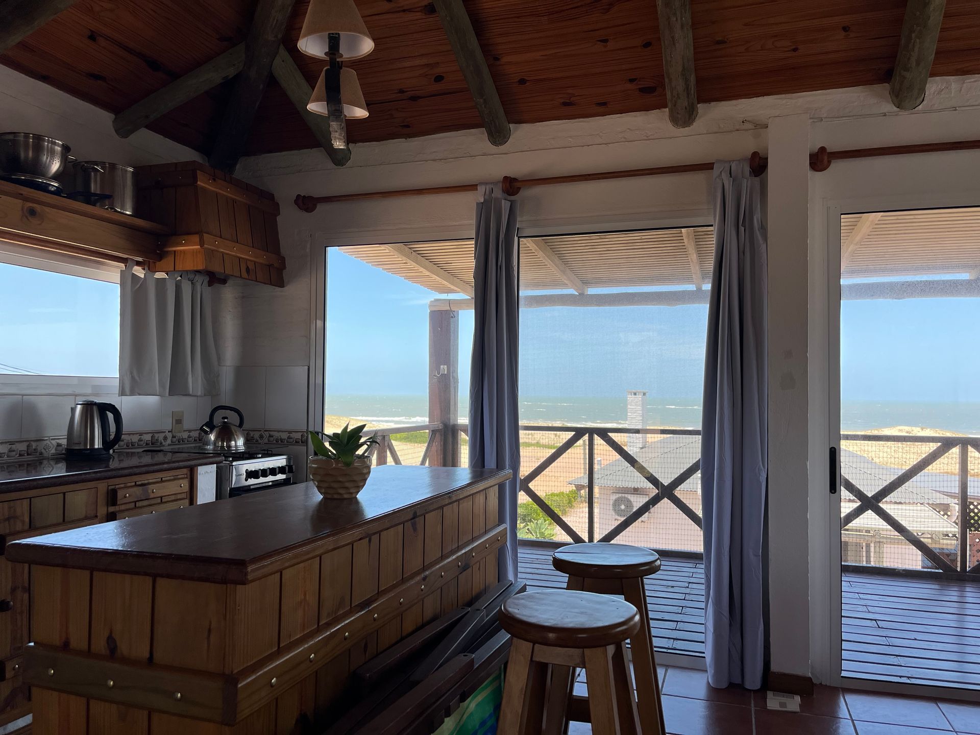 A kitchen with a wooden island and stools and a view of the ocean.