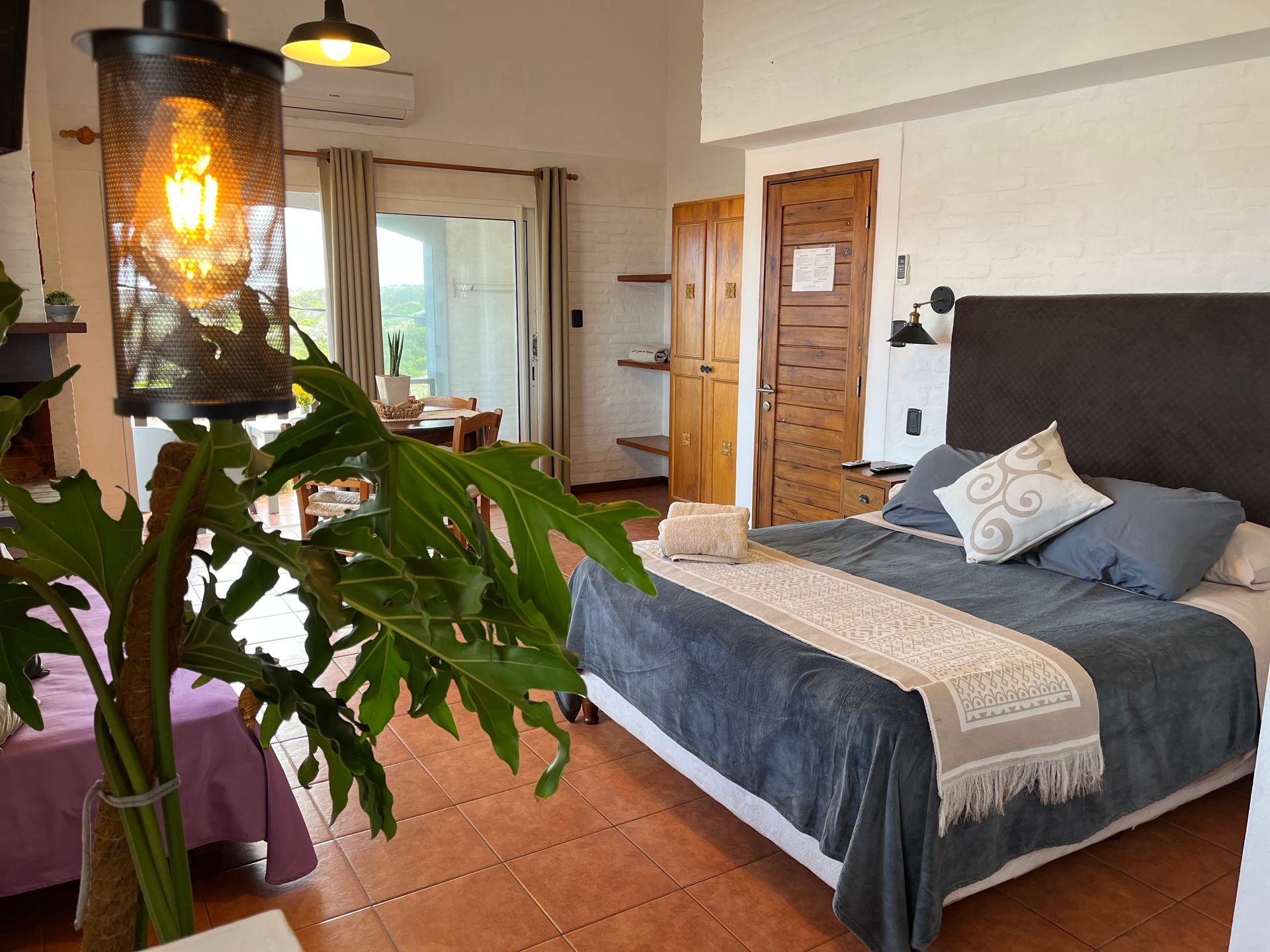 A bedroom with a large bed and a plant in the foreground.