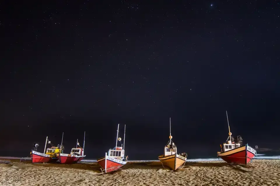 A row of boats are lined up on a beach at night.