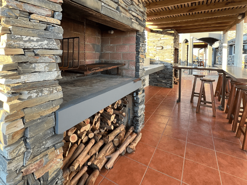 A large pile of logs is sitting next to a stone wall in a room.