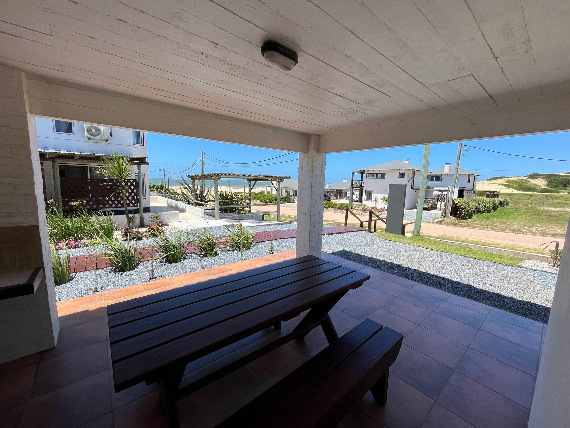 A wooden picnic table with benches under a covered porch.