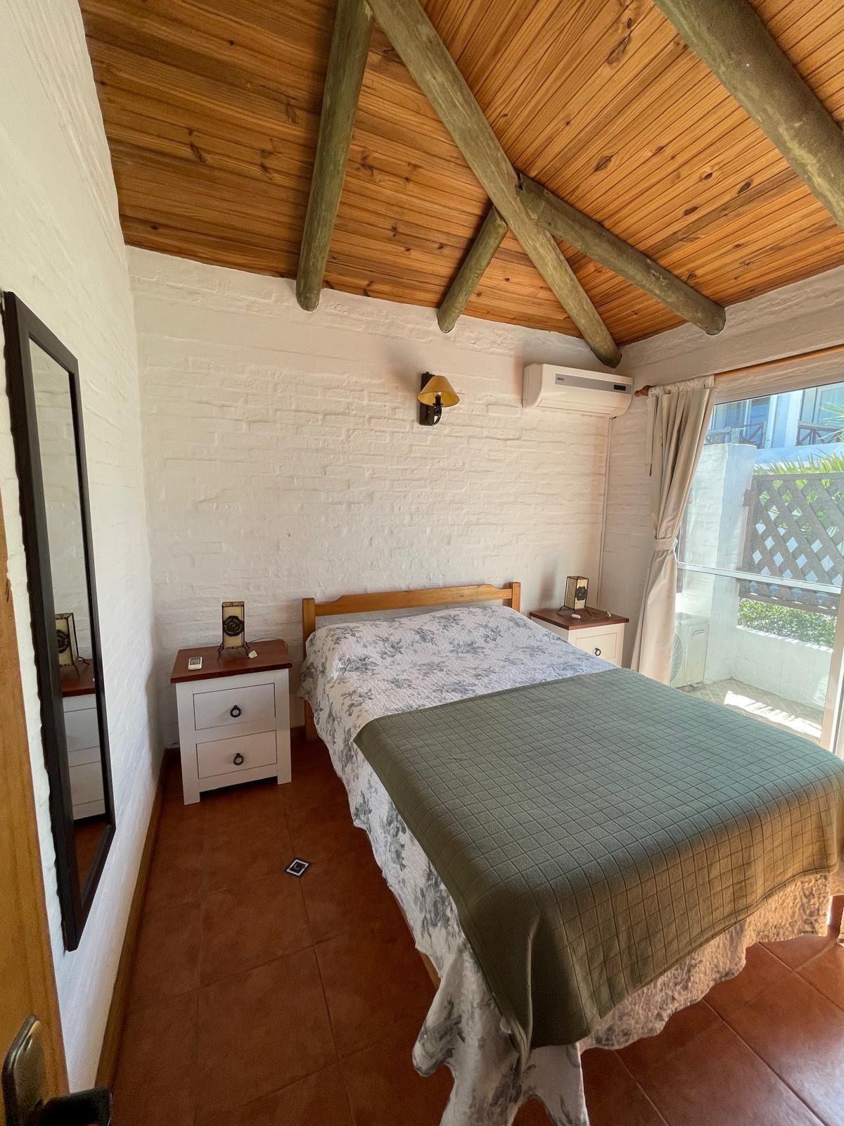 A bedroom with a bed , nightstands , a mirror and a wooden ceiling.