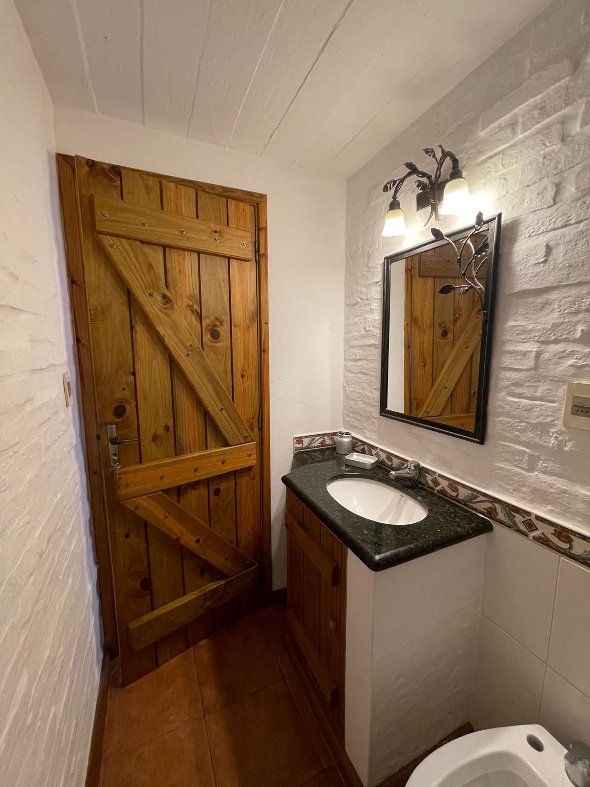 A bathroom with a sink , toilet , mirror and wooden door.