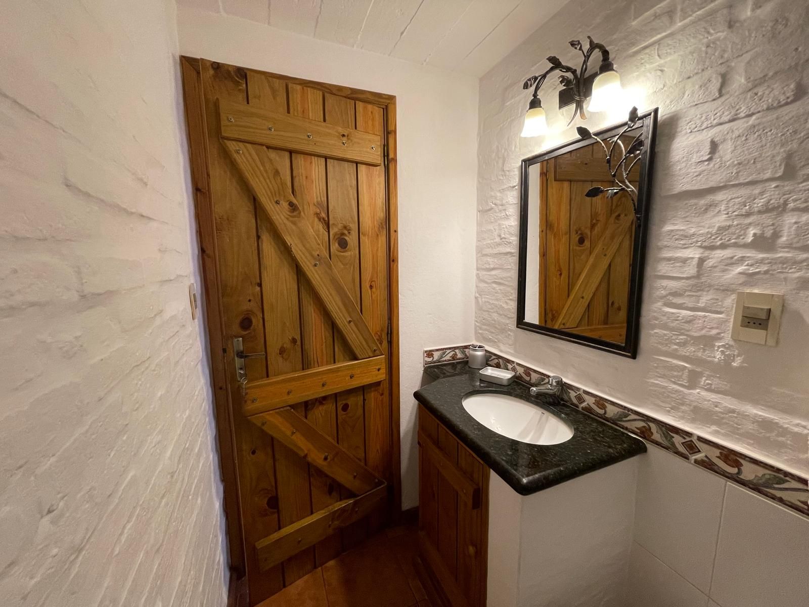 A bathroom with a wooden door , sink and mirror.