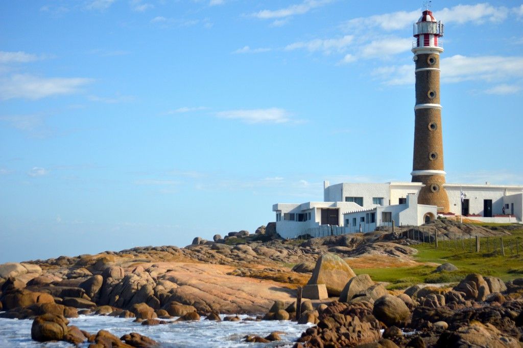 A lighthouse is sitting on top of a rocky hill next to the ocean.