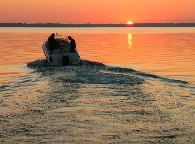 A boat is floating on the water at sunset.