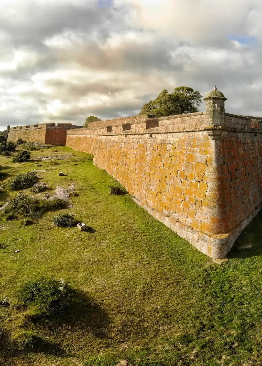 A large brick wall is surrounded by grass on a hill.