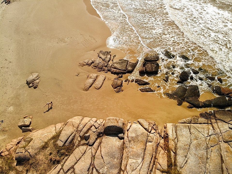 An aerial view of a rocky beach with waves crashing on the rocks.