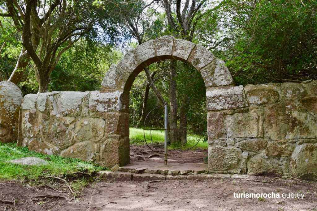 A stone archway leading to a forest with trees in the background.