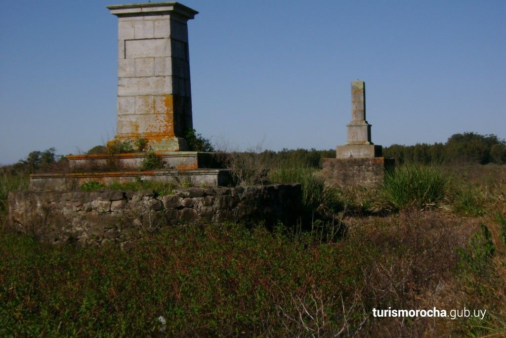 A stone pillar is in the middle of a grassy field.