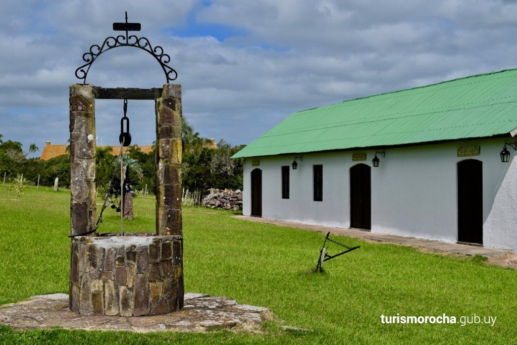 A well with a cross on top of it in front of a building