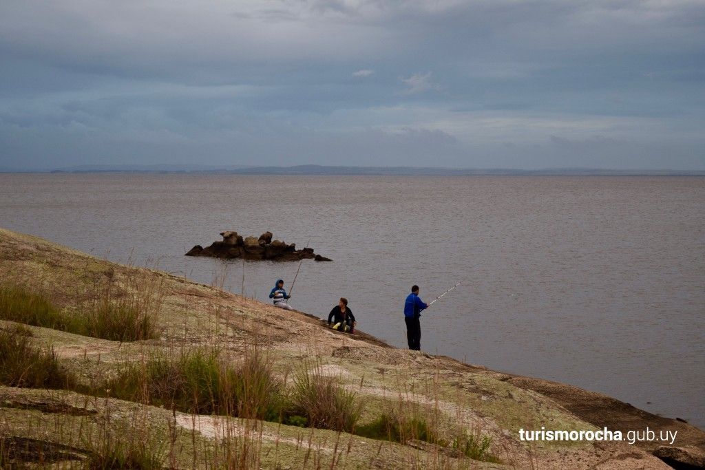 Three people are fishing on the shore of a lake.