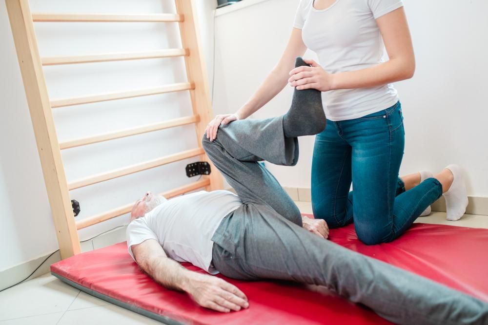 A Woman Is Stretching A Man 's Leg On A Red Mat — Mark Coulton Cardiff Physiotherapy Centre In Cardiff, NSW
