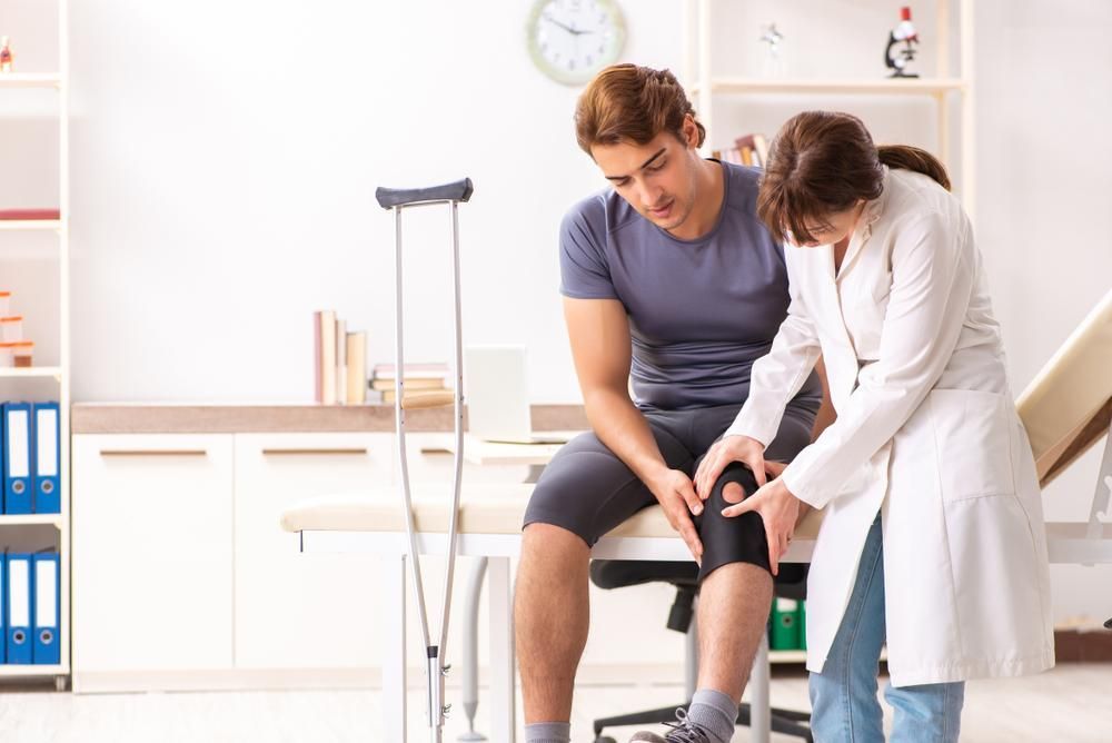 A Doctor Is Examining A Patient 's Knee In A Hospital — Mark Coulton Cardiff Physiotherapy Centre In Cameron Park, NSW