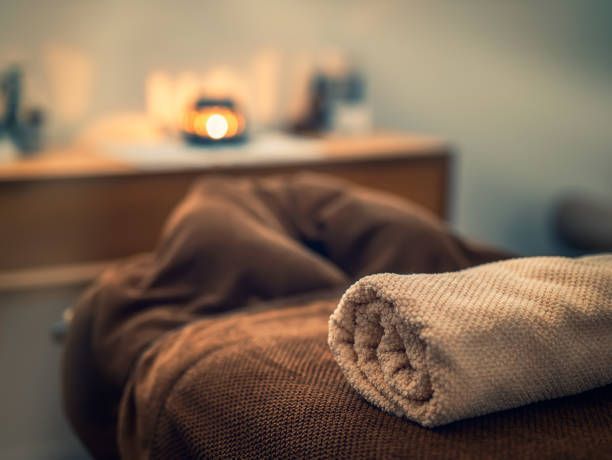 A towel is rolled up on a bed with a candle in the background.