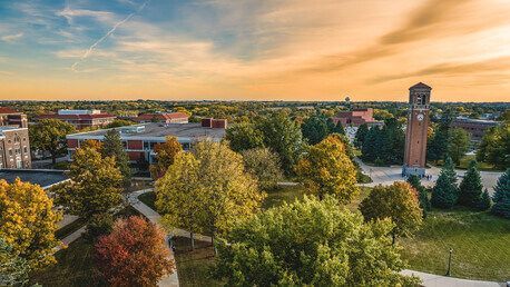Sunset over a tree-lined campus with buildings and a tall clock tower