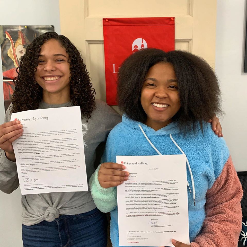 Smiling image of two young females, one is holding papers 