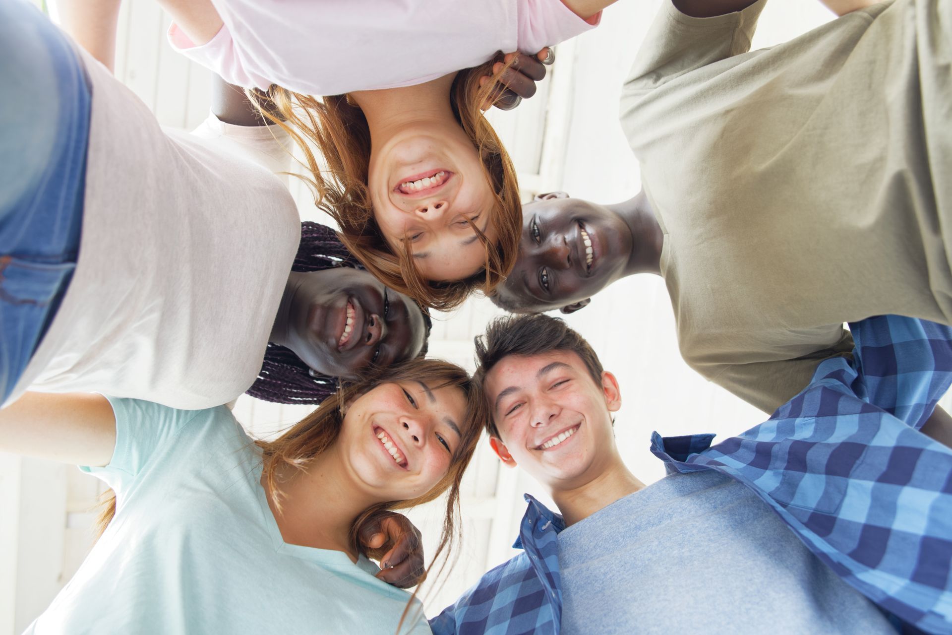 Five people huddle in a circle, smiling down at the camera outdoors.
