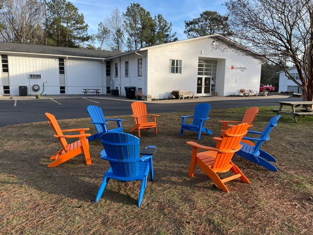Colorful Adirondack chairs in a grassy yard outside a white house with a large garage and windows.