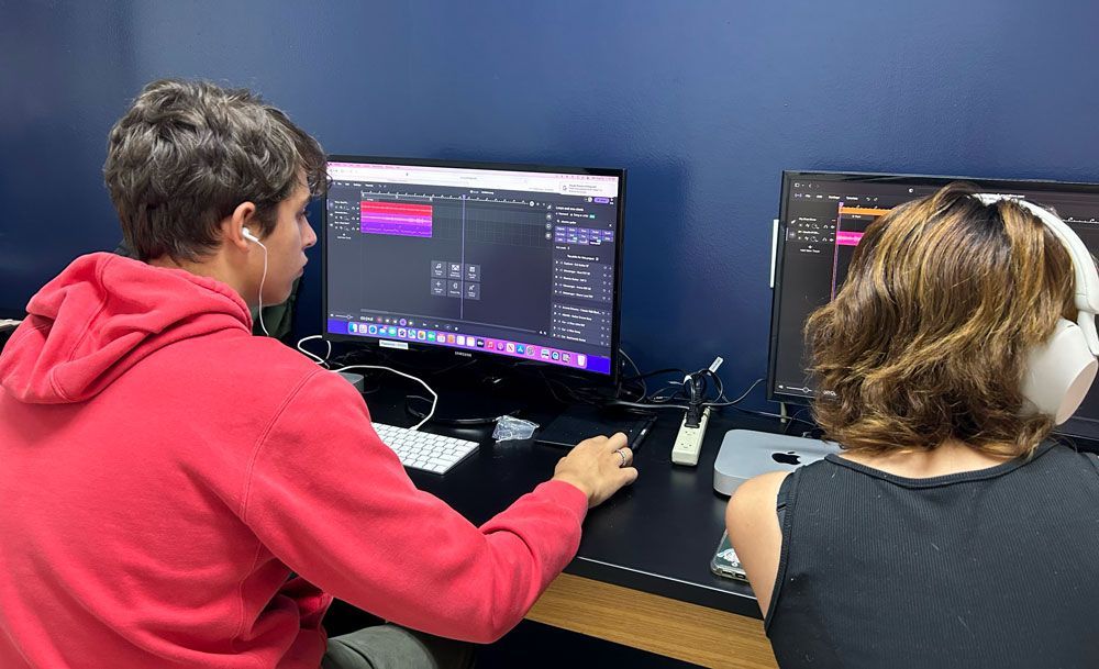 Two people at desktop computers in a blue room, working on screens showing software.