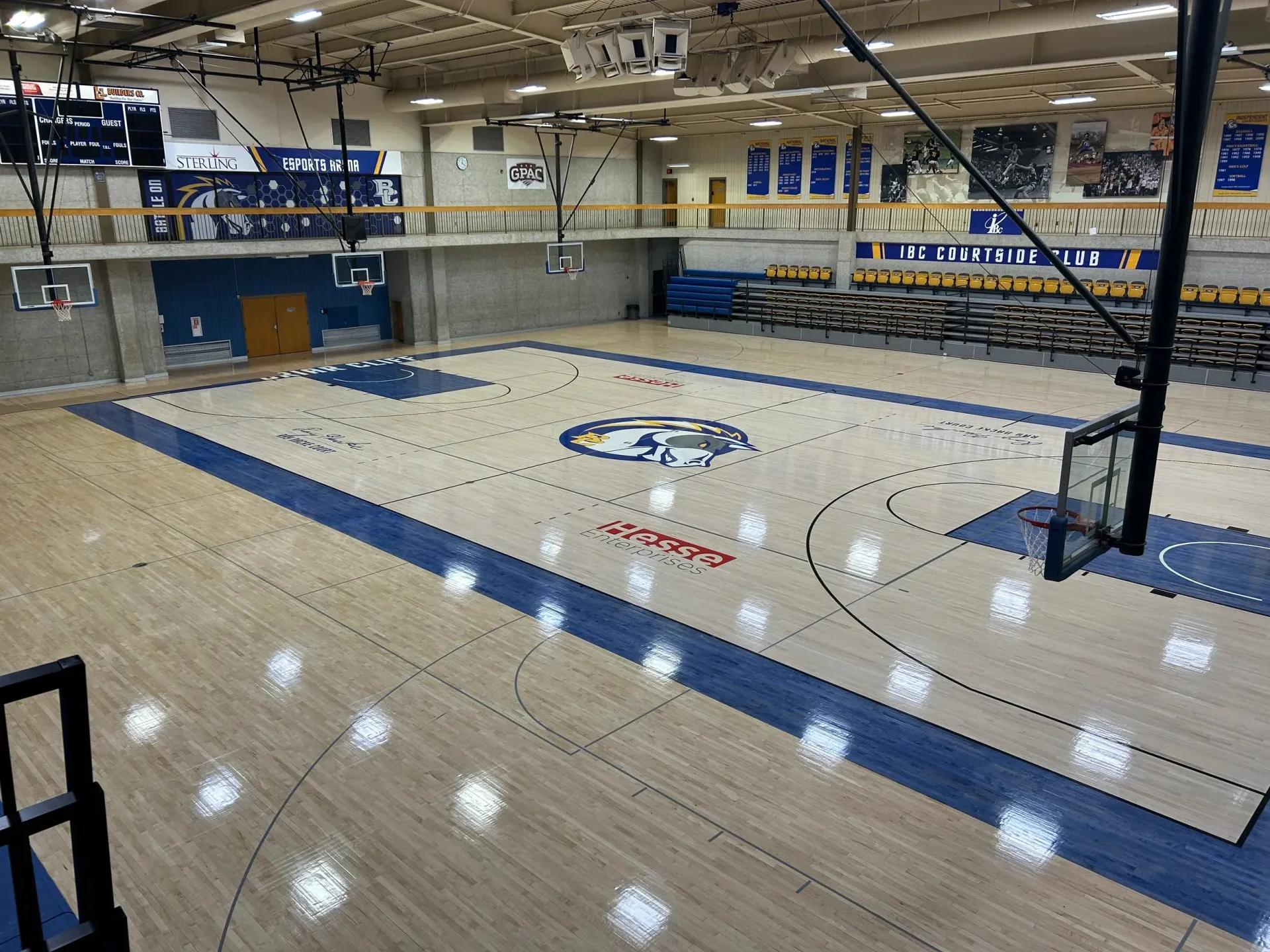 Empty indoor basketball court with blue-and-white markings and bleachers in a gymnasium