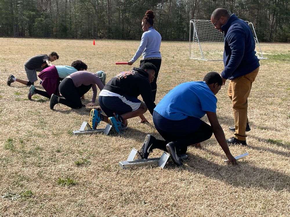 People crouching at a starting line during an outdoor field exercise near a soccer goal.