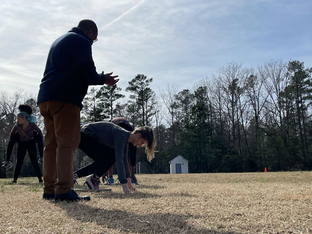 People crouch at the starting line on a grassy field during an outdoor race start.