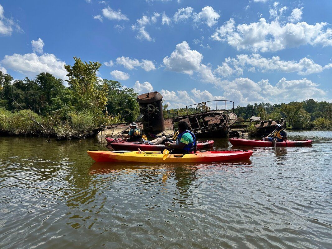 Two kayaks on a calm river, carrying gear, under a blue sky with scattered clouds.