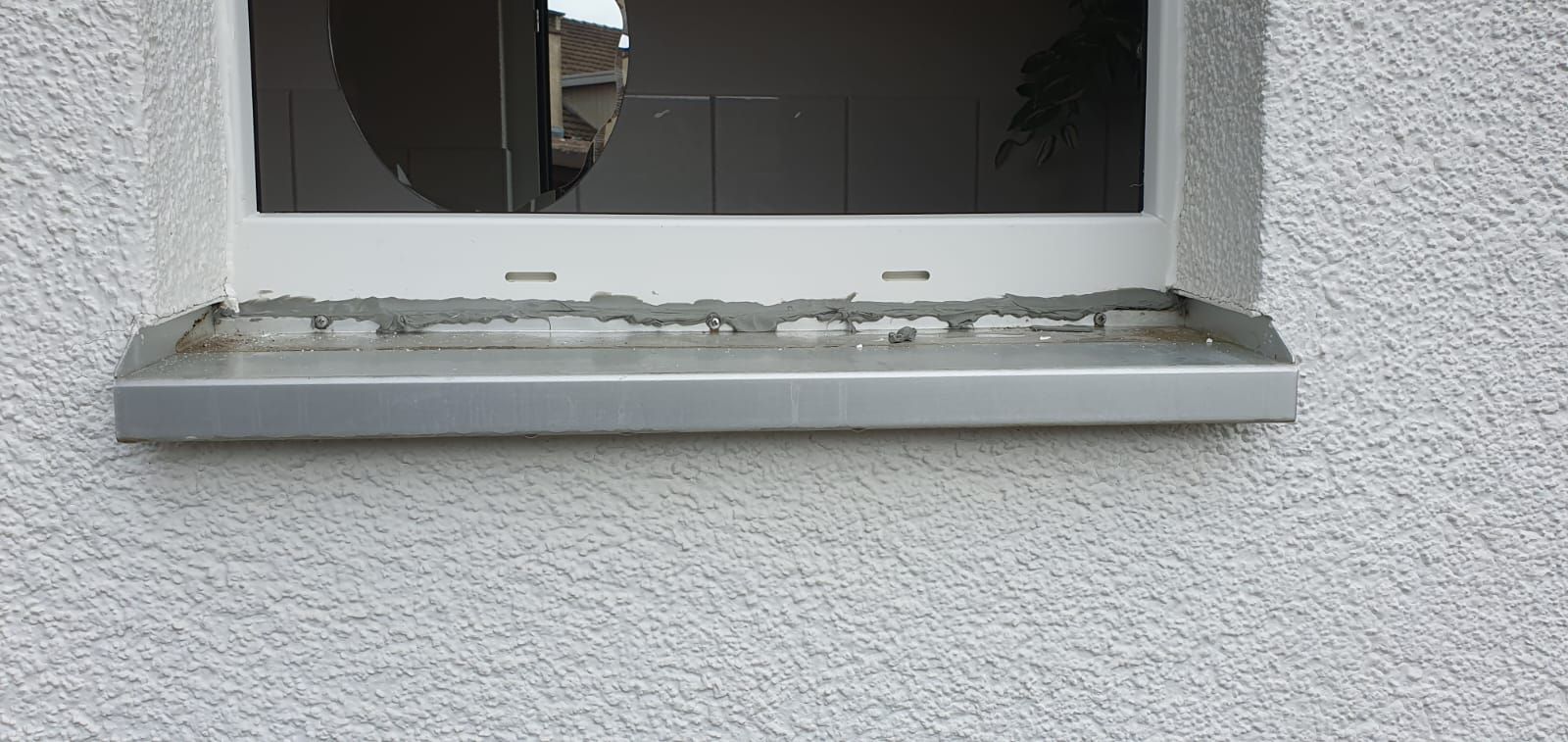 Ein Fenster mit einer Metallbank an einer grauen Wand.