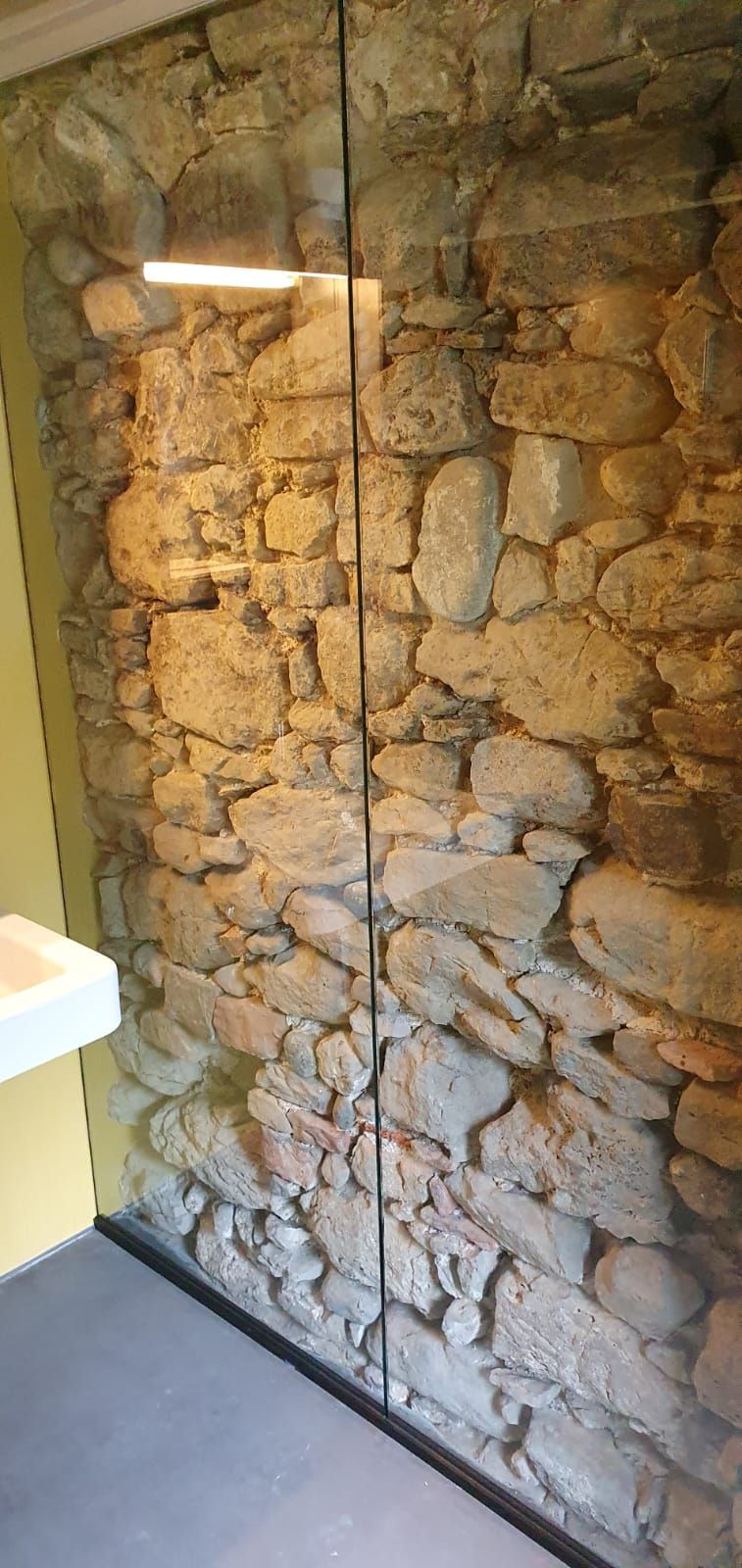 Ein Badezimmer mit einer Steinwand und einer Glaswand.