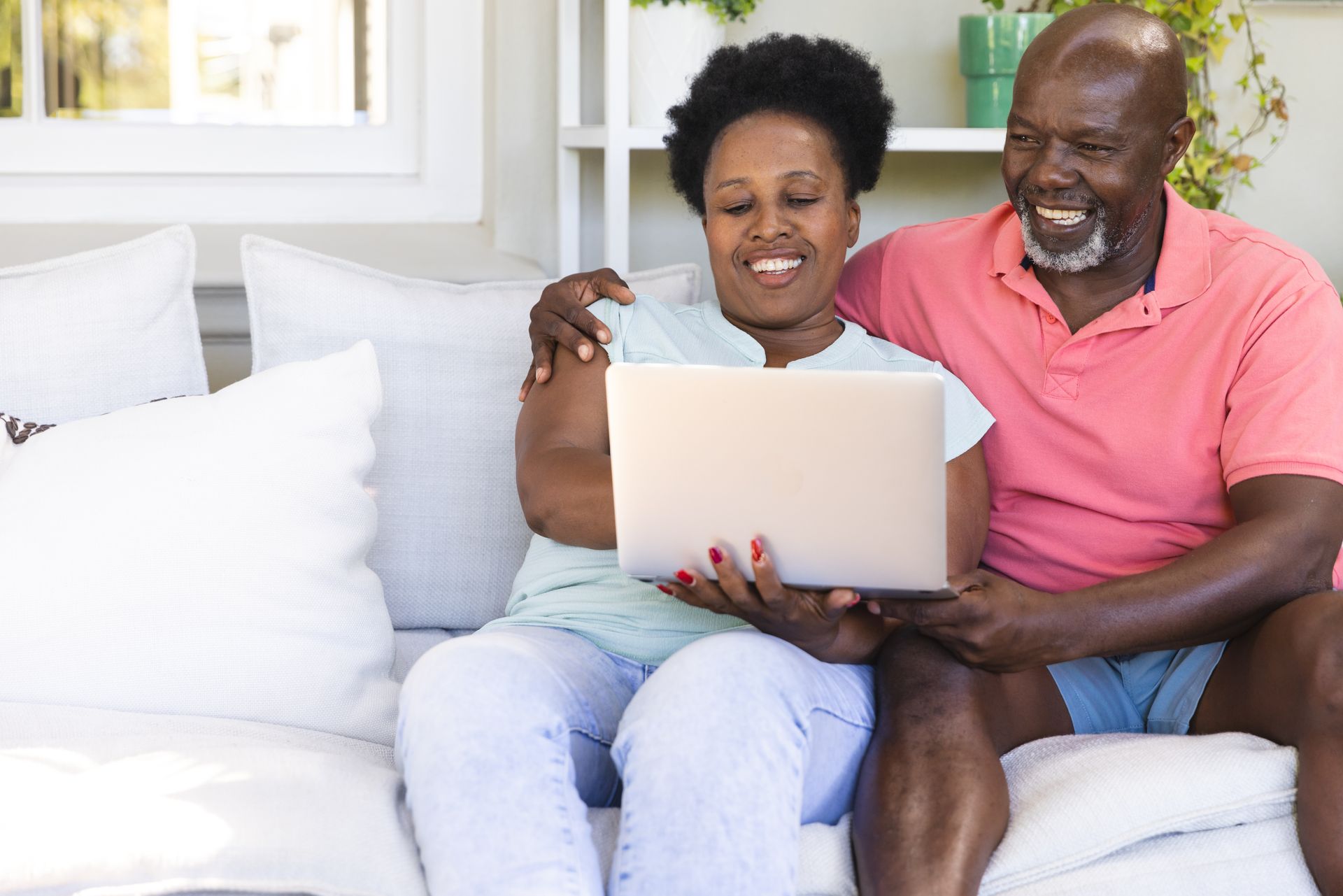 Couple smiling on a white couch, looking at a laptop together in a bright living room