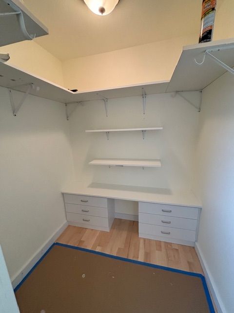 White built-in desk and shelves in a small room with light wood floors and blue painter's tape.
