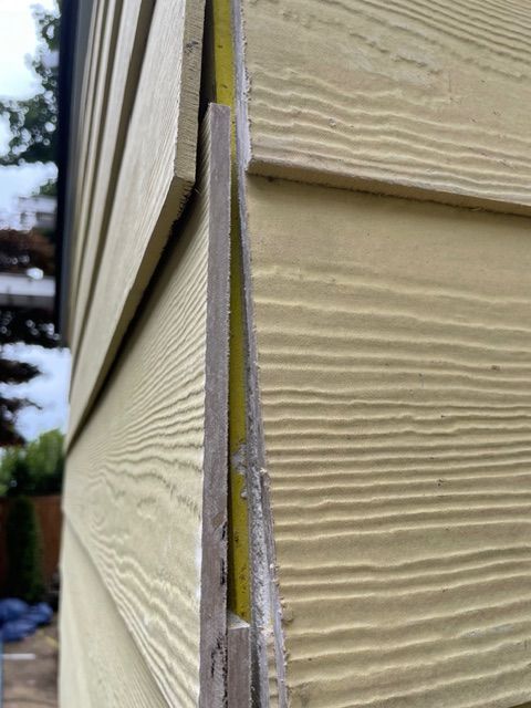 Yellow siding with a gap and measuring tape visible.