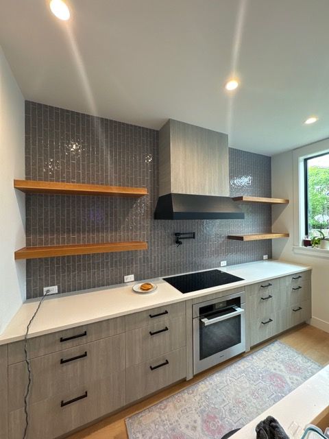 Modern kitchen with gray cabinets, wood shelves, and a gray tiled backsplash.