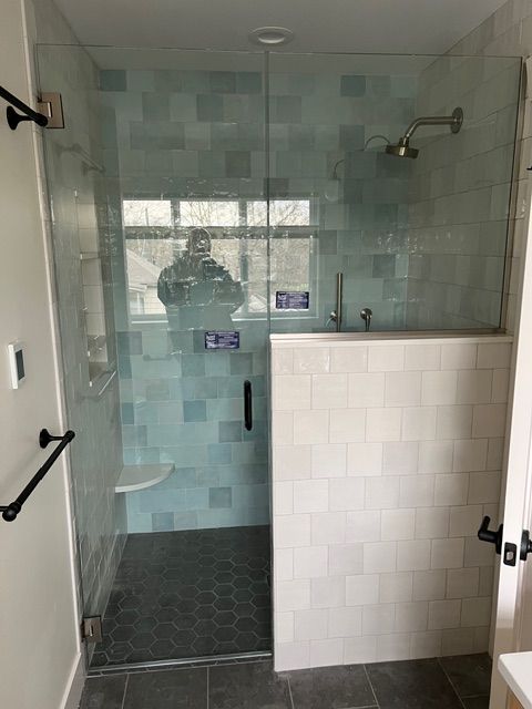 Modern shower with glass doors, blue tile, white tile half wall, and dark floor.