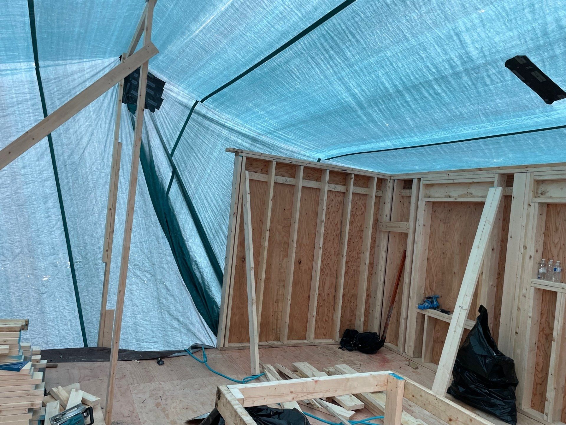 Interior framing of a room under a blue tarp shelter.