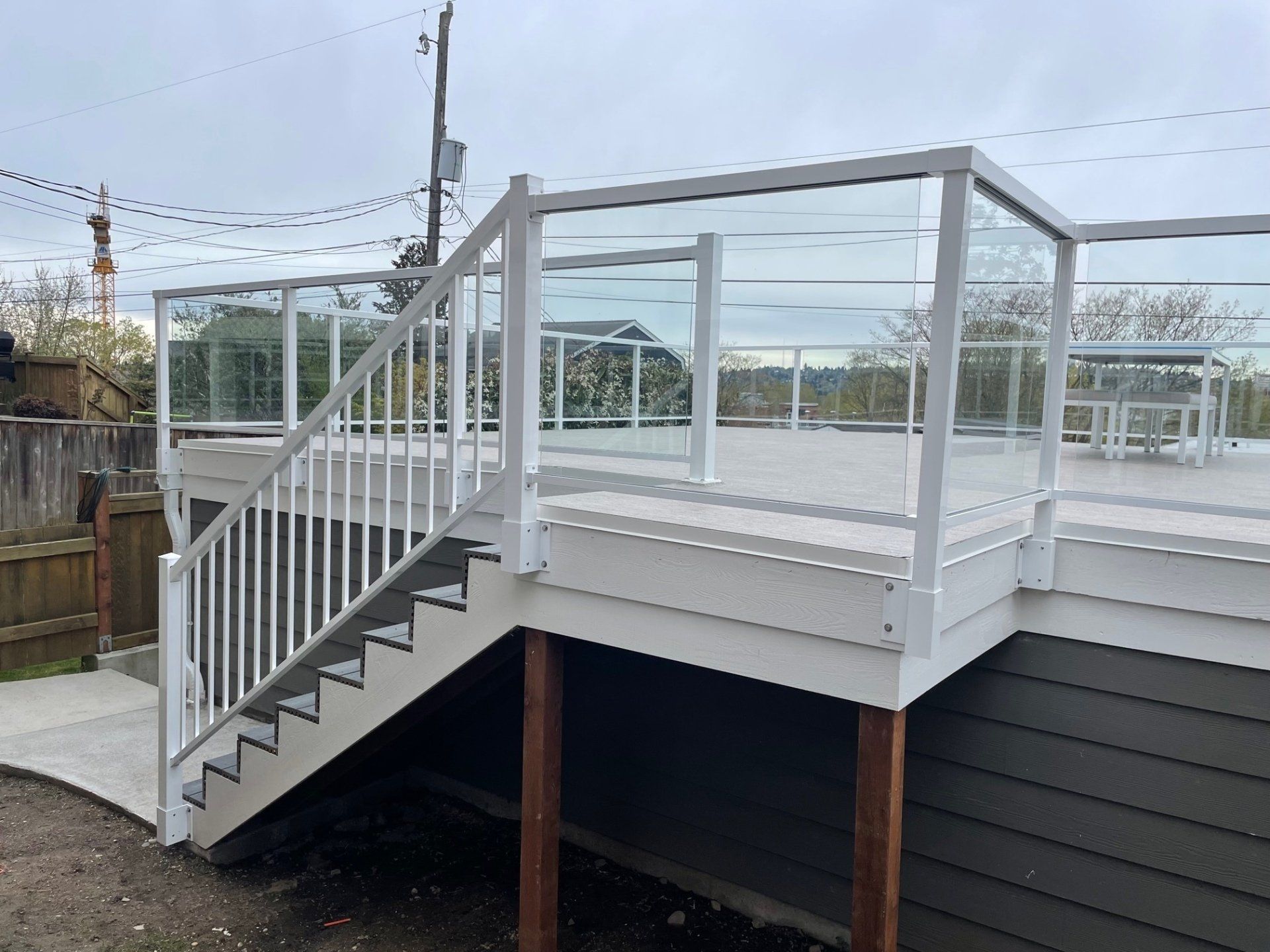 White deck with glass railings and stairs leading to a concrete path. Gray siding and cloudy sky.